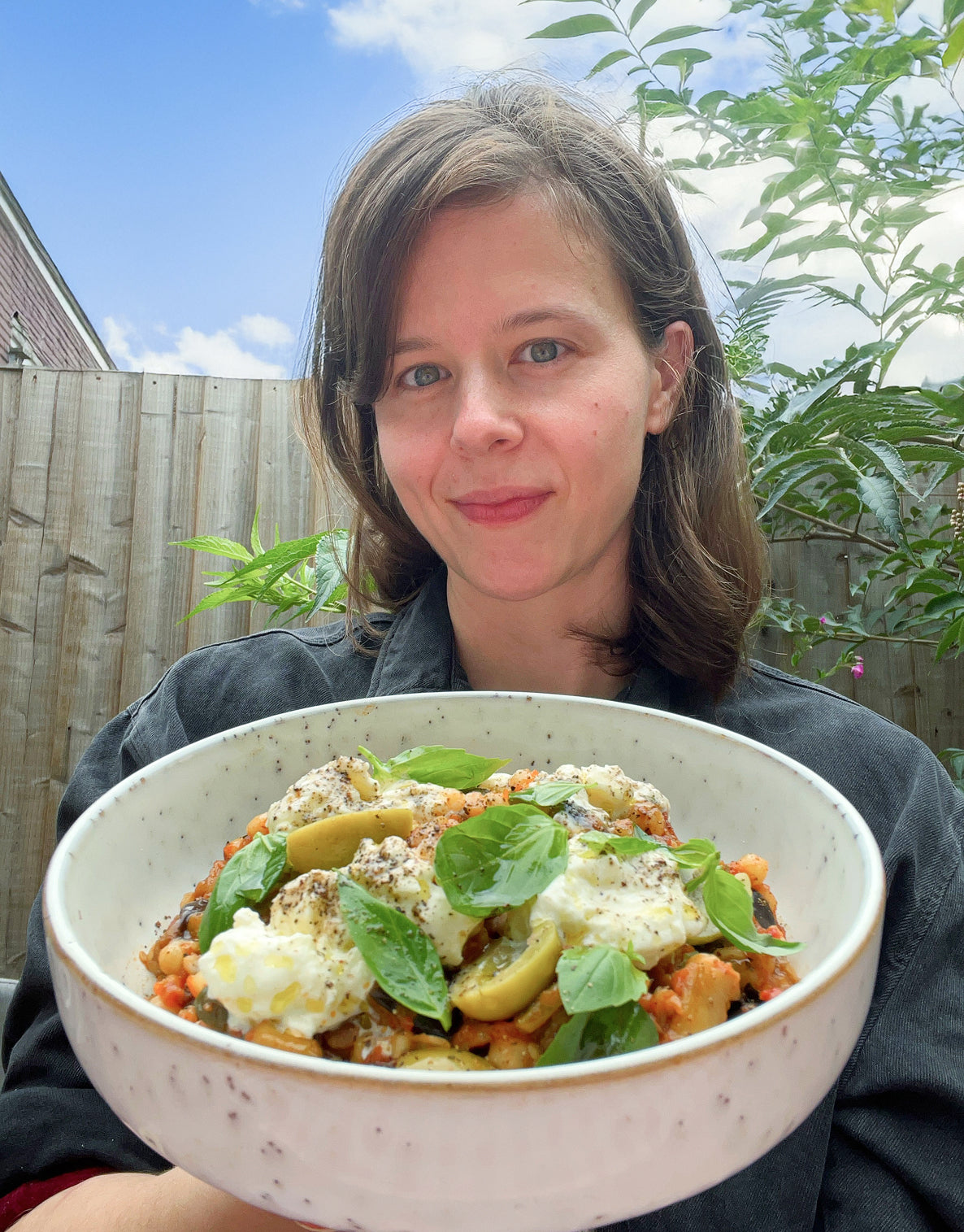 Person holding a bowl of salad outdoors with greenery in the background